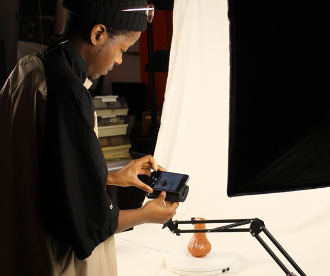 Professional 3D scanning setup featuring a person photographing a ceramic object on a turntable under studio lights.